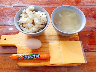 芝士火腿鸡蛋汤泡饭,首先我们准备好所有食材！米饭是前一晚剩下的！菜汤也是前一晚剩下的，如果你没有，可以用饮用水替代！火腿肠随你喜欢用哪一种，我这里用的是有玉米粒的！